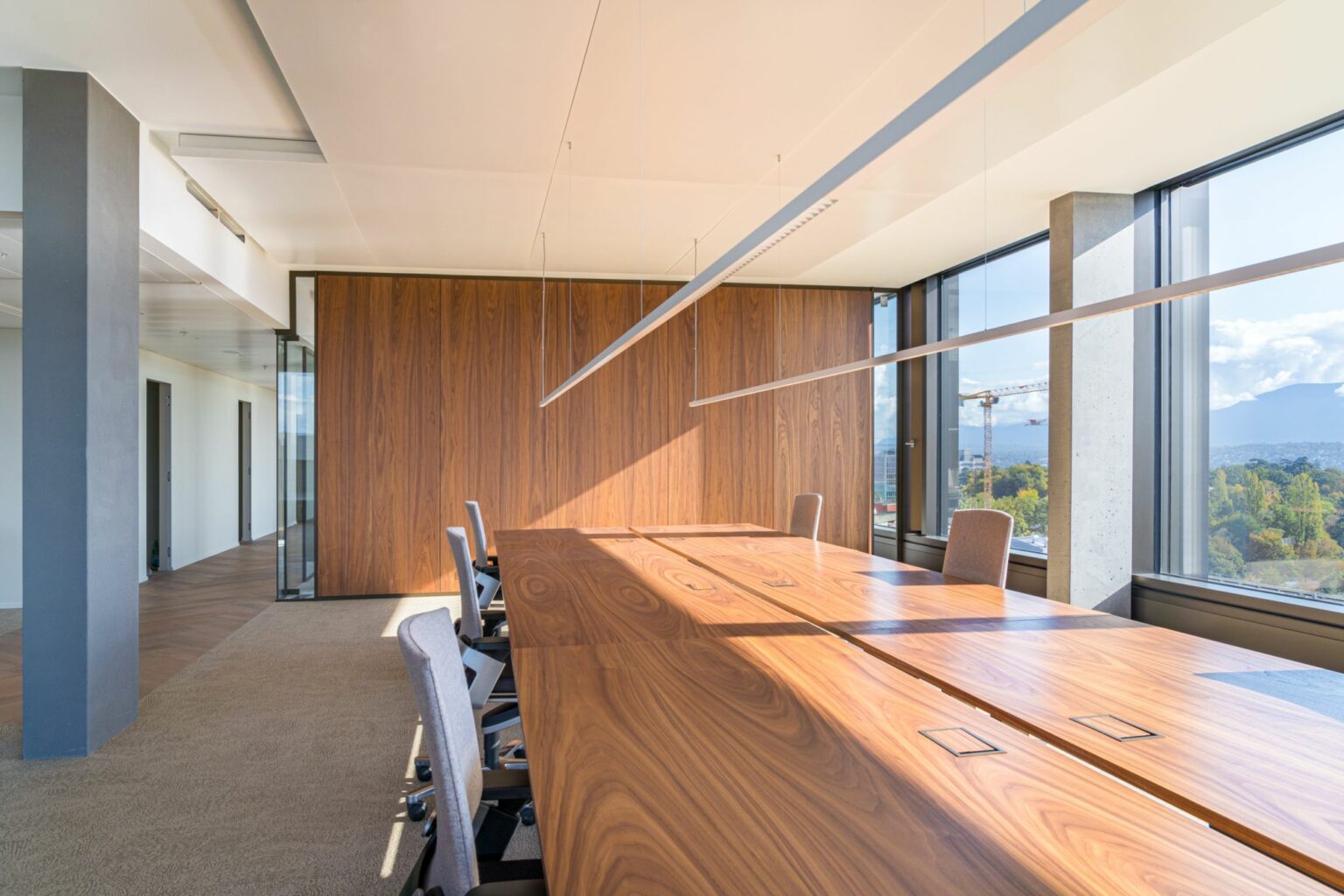 Espace de réunion lumineux avec grande table en bois, lumière naturelle et vue dégagée, conçu pour améliorer le confort de travail.