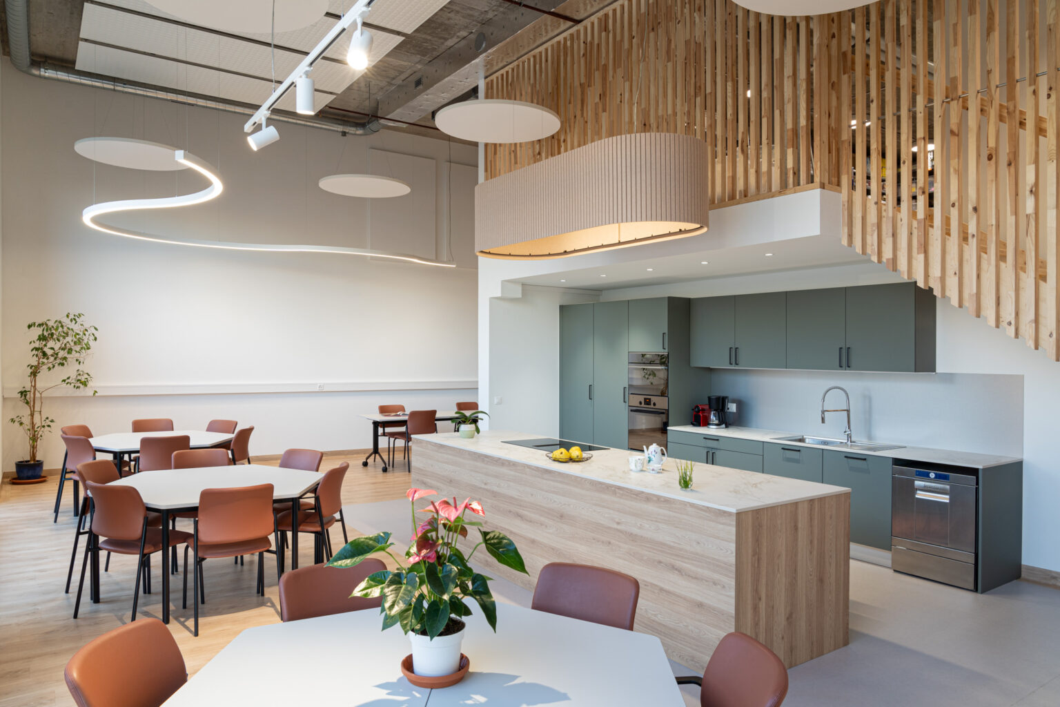 Grande salle polyvalente avec cuisine ouverte, tables de convivialité et architecture intérieure épurée à Genève.