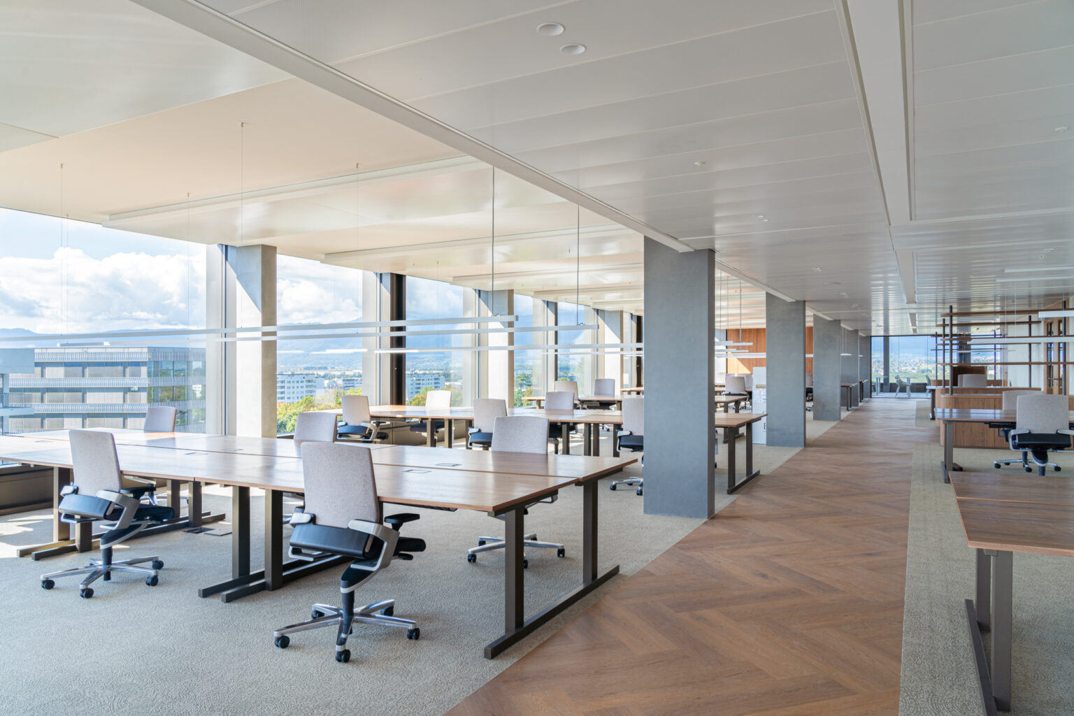 Aménagement d'un open space spacieux avec des îlots de bureaux en bois, des chaises ergonomiques et un sol mixte moquette et parquet.