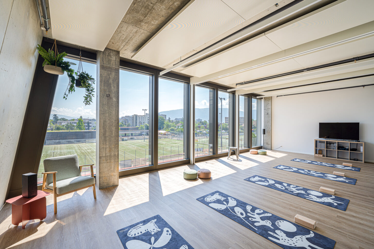 Vaste espace lumineux aménagé avec plusieurs tapis de yoga alignés face à de grandes baies vitrées et un écran de présentation.