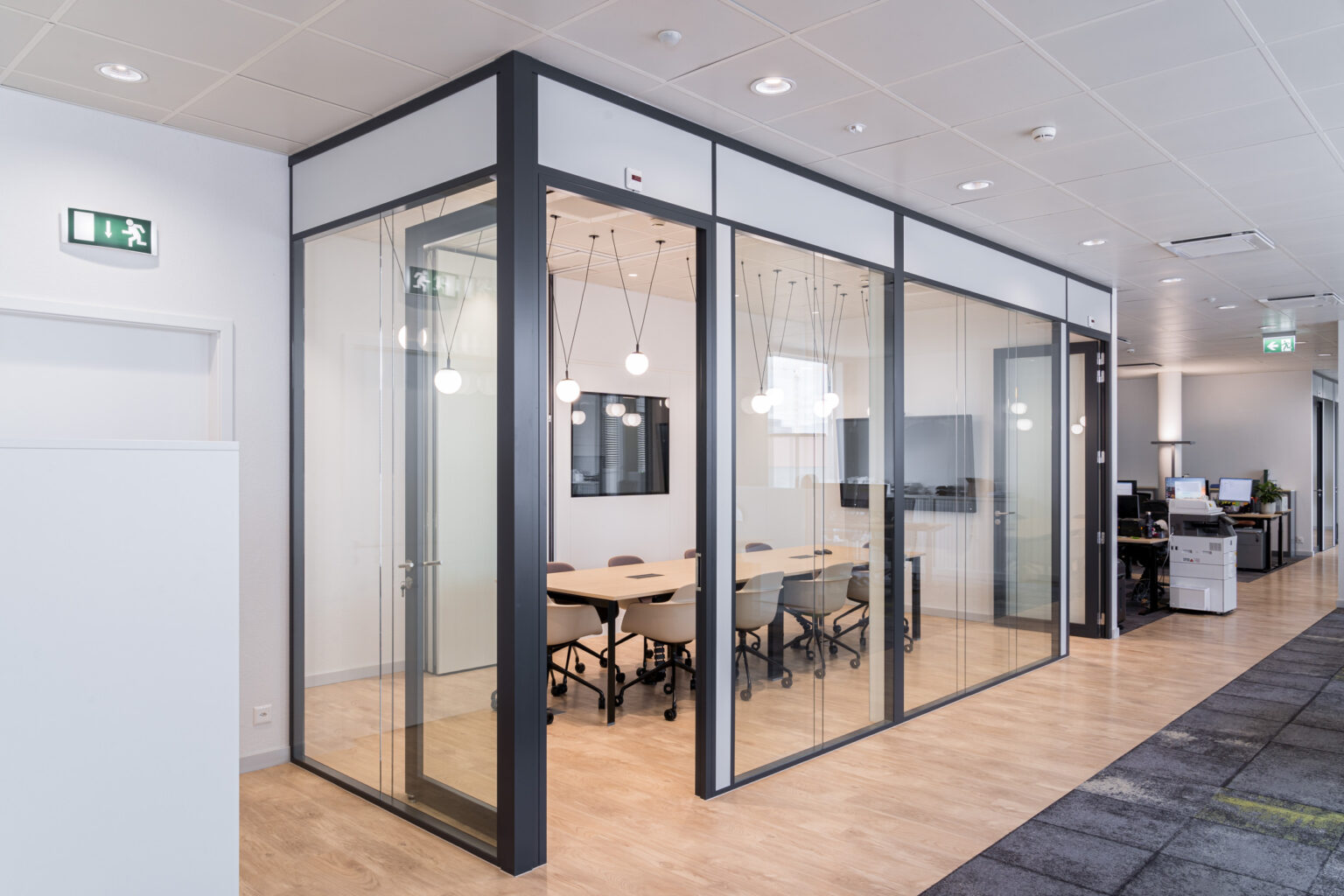 Vue extérieure d'un espace de réunion vitré à structure métallique noire, s'intégrant au cœur d'un plateau de bureaux contemporain.