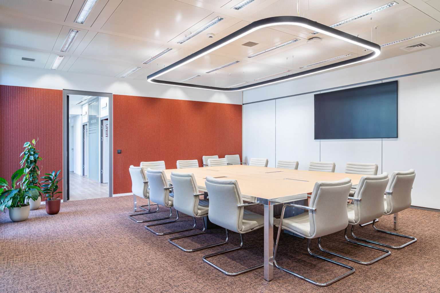 Salle de réunion contemporaine équipée d'une grande table de conférence, de fauteuils ergonomiques, d'un écran mural et d'un éclairage suspendu design.