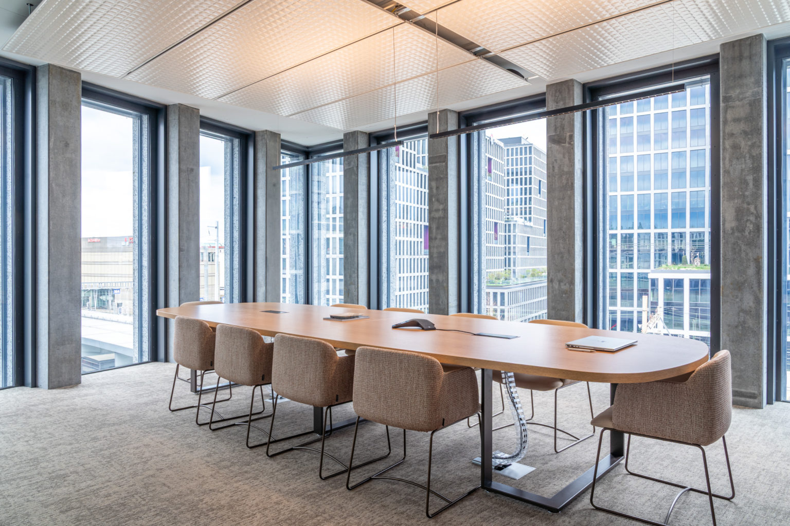 Grande table de réunion entourée de fauteuils tapissés, bénéficiant d'une abondante lumière naturelle grâce aux façades vitrées.