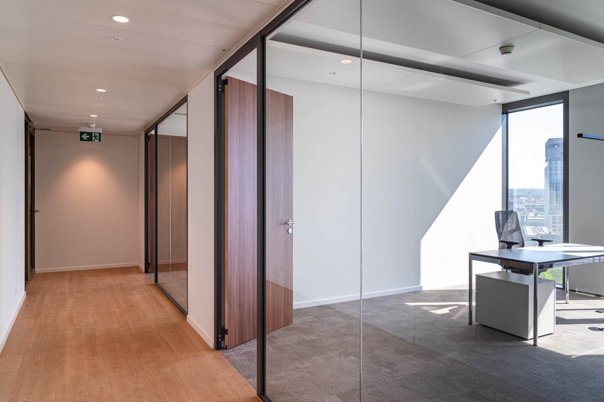 Bureau individuel aménagé à Genève avec cloisons vitrées, portes en bois, revêtement de sol mixte et lumière naturelle.