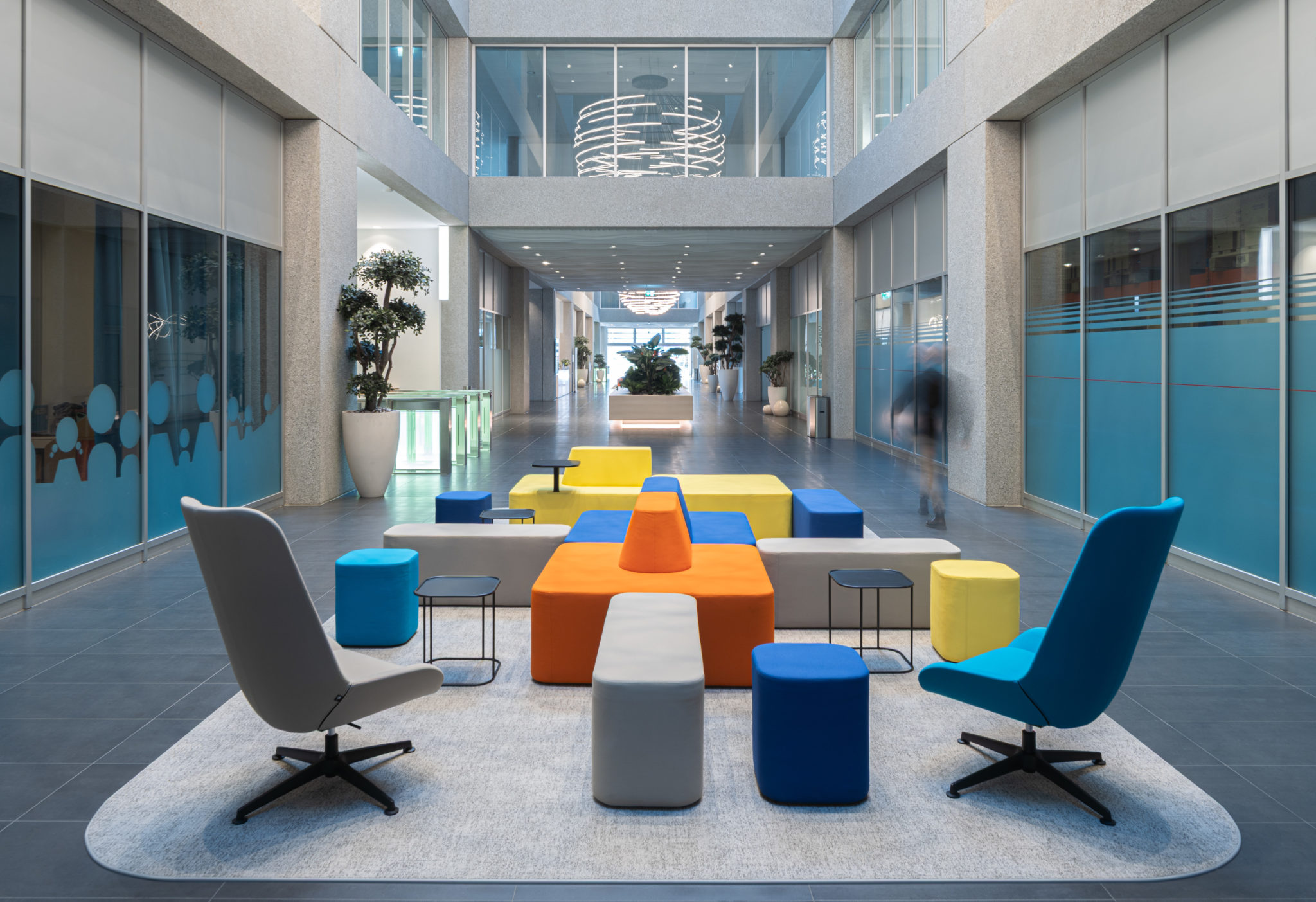Mobilier d'accueil coloré installé au cœur d'un atrium entouré de bureaux vitrés.