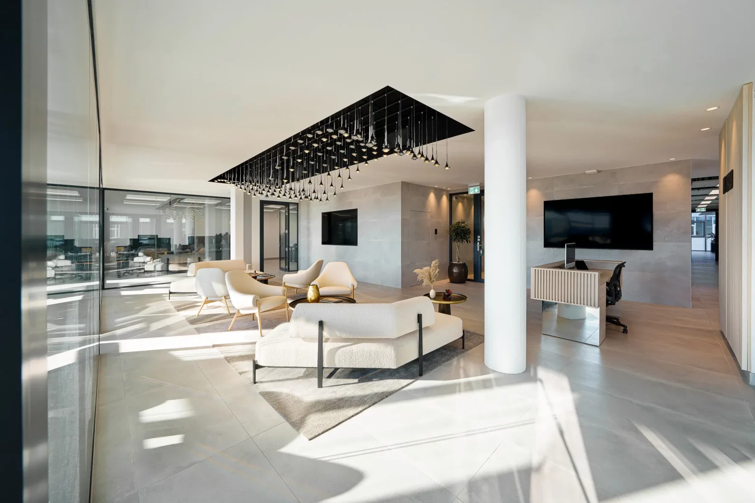Espace d'accueil de bureaux modernes avec salon d'attente, mobilier design, suspension lumineuse contemporaine et grandes cloisons vitrées.
