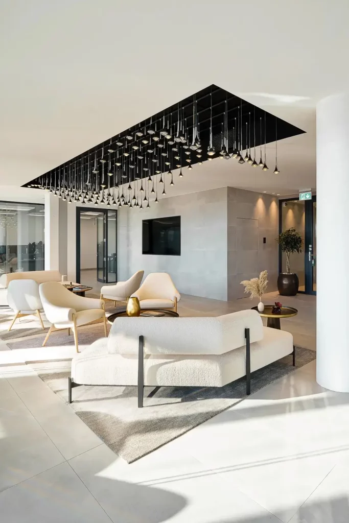 Espace d'accueil de bureaux modernes avec salon d'attente, mobilier design, suspension lumineuse contemporaine et grandes cloisons vitrées.