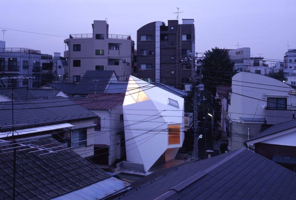 Micro-maison japonaise ultra-moderne aux formes géométriques facettées, illuminée au crépuscule dans un quartier résidentiel de Tokyo.