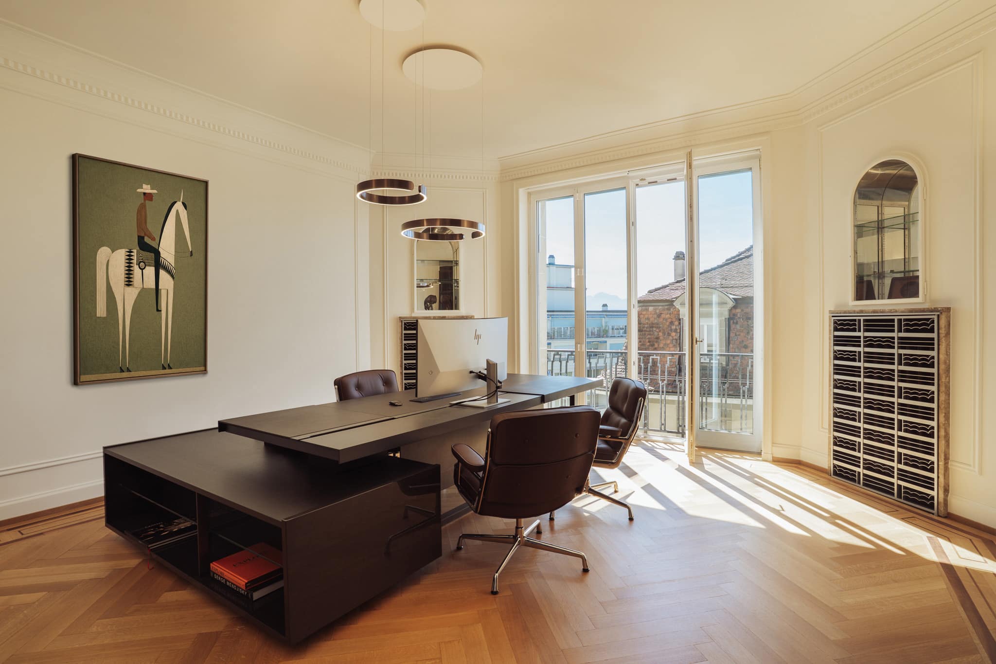 Bureau de direction, composé d’un grand plan de travail en bois, de fauteuils en cuir et de portes-fenêtres.
